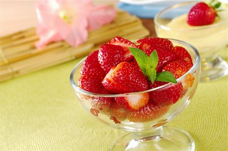 Fresh strawberries cut in half with mint leaf as garnish in a glass bowl  with a cream cheese dessert and gladiolus in the background (Selective Focus, Focus on the strawberries in the front and the mint leaf) Foto de stock - Royalty-Free Super Valor e Assinatura, Número: 400-04359725