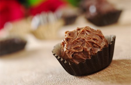 Closeup of a milk chocolate truffle with wrapping, with other truffles and red roses in the background photographed on wood (Very Shallow Depth of Field, Focus on the front of the first praline) Stock Photo - Budget Royalty-Free & Subscription, Code: 400-04350270