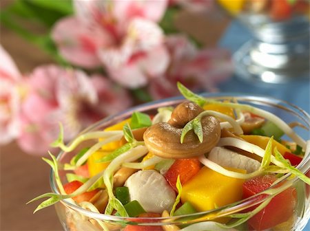 raw cashews - Fresh Asian salad with chicken, mango, cucumber, bean sprouts, red bell pepper and peanuts in glass bowl with inca lily in the back (Selective Focus, Focus on the cashew nut and the bean sprout on the top) Photographie de stock - Aubaine LD & Abonnement, Code: 400-04352391