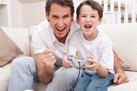 Happy man and boy, father and son, having fun playing video console games together, the young boy has the handset controller while dad is cheering. Stock Photo - Budget Royalty-Free & Subscription, Code: 400-04366146