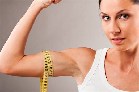 sporty woman is measuring her biceps on grey background Photographie de stock - Aubaine LD & Abonnement, Code: 400-04361221