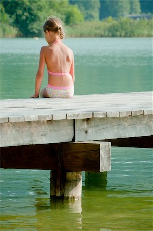 Cute little girl sitting on a pier and looking at the water. Vertical view Foto de stock - Super Valor sin royalties y Suscripción, Código: 400-04373087