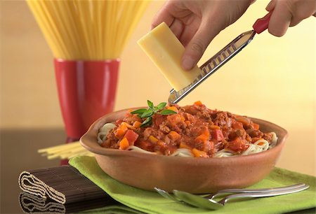 Grating cheese over spaghetti bolognaise with minced meat, carrot, tomato and onion, garnished with oregano leaf (Selective Focus, Focus on the oregano leaves on the spaghetti and the cheese held in the hand) Stockbilder - Microstock & Abonnement, Bildnummer: 400-04381966