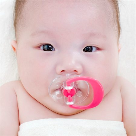 Asian baby girl with a soother in her mouth lying on bed Photographie de stock - Aubaine LD & Abonnement, Code: 400-04382278