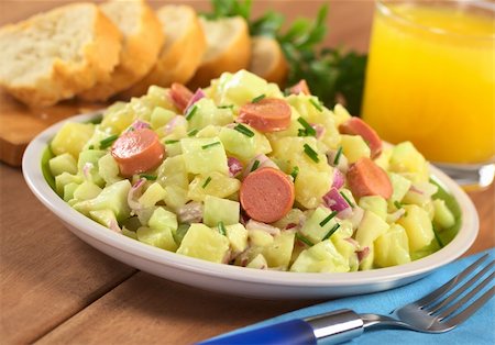 simsearch:400-04855321,k - Fresh potato salad made of potato, cucumber, red onion and chives with a mayonnaise dressing and sausage slices with orange juice and baguette slices in the back (Selective Focus, Focus one third into the salad, on the sausage slice in the middle) Stock Photo - Budget Royalty-Free & Subscription, Code: 400-04394325