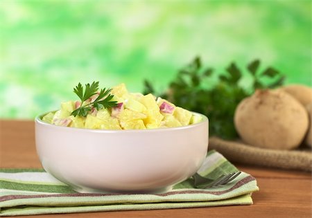Potato salad made of cooked potatoes, red onions and cucumber, seasoned with a mayonnaise dressing and garnished with a parsley leaf (Selective Focus, Focus on the front of the salad and the leaf) Foto de stock - Super Valor sin royalties y Suscripción, Código: 400-04394322