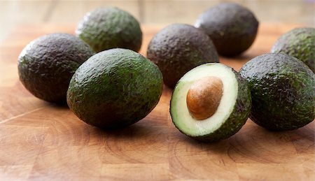 simsearch:400-07718938,k - Loose avocados on a wooden chopping board with one cut in half Fotografie stock - Microstock e Abbonamento, Codice: 400-04398181