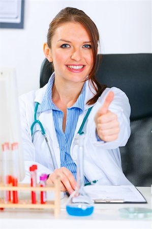 Smiling medical doctor woman sitting at office table and showing thumbs up gesture Stock Photo - Budget Royalty-Free & Subscription, Code: 400-04390408