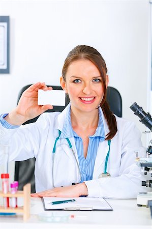 simsearch:400-04925813,k - Smiling medical doctor woman sitting at office table and holding blank business card Stock Photo - Budget Royalty-Free & Subscription, Code: 400-04390417