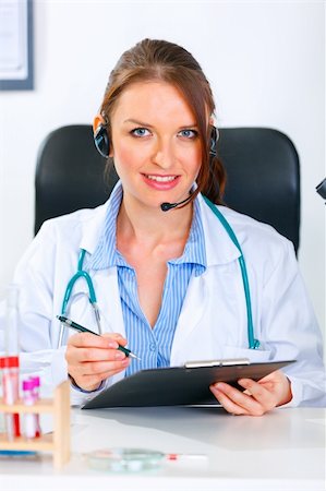 simsearch:400-04925813,k - Smiling medical doctor woman with headset sitting at office table and holding  clipboard Stock Photo - Budget Royalty-Free & Subscription, Code: 400-04390418