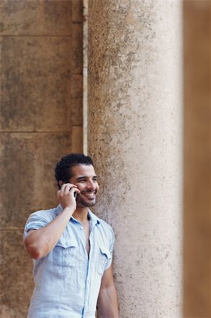 simsearch:400-04391064,k - mid adult hispanic man talking on mobile phone and leaning on columns outdoors. Verticl shape, side view, copy space Stock Photo - Budget Royalty-Free & Subscription, Code: 400-04391068