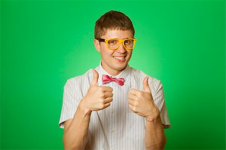 sunny_baby (artist) - Handsome young man in a shirt and yellow glasses, bow tie on a green background smiling at the camera. Two thumbs up Foto de stock - Royalty-Free Super Valor e Assinatura, Número: 400-04392237