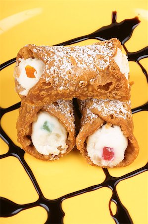 simsearch:400-05341443,k - Close-up of original mini sicilian cannoli over a yellow plate. These tube-shaped pastries are made of fried shells filled with a sweet mixture of ricotta cheese, chocolate, candied fruit and sprinkled with icing sugar. Stockbilder - Microstock & Abonnement, Bildnummer: 400-04405379