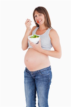 Attractive pregnant woman eating a cherry tomato while holding a bowl of salad against a white background Stock Photo - Budget Royalty-Free & Subscription, Code: 400-04406030