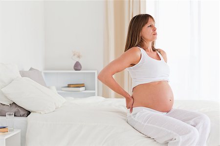 Beautiful pregnant female having a back pain while sitting on a bed in her apartment Stock Photo - Budget Royalty-Free & Subscription, Code: 400-04406074