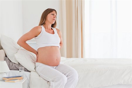 Attractive pregnant female having a back pain while sitting on a bed in her apartment Stock Photo - Budget Royalty-Free & Subscription, Code: 400-04406075