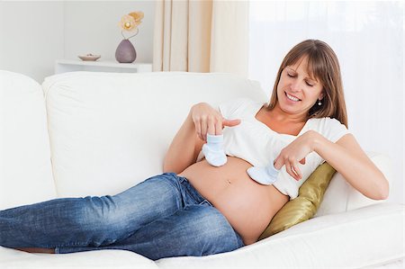 Beautiful pregnant woman playing with baby shoes while lying in her living room Stock Photo - Budget Royalty-Free & Subscription, Code: 400-04406114