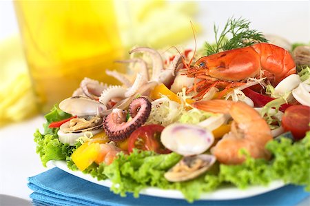 simsearch:400-04854606,k - Seafood salad with shrimp, clams, octopus tentacles, calamari rings and prawns with a variety of vegetables with white wine in the back (Selective Focus, Focus on the shrimp on top of the salad) Foto de stock - Royalty-Free Super Valor e Assinatura, Número: 400-04406470