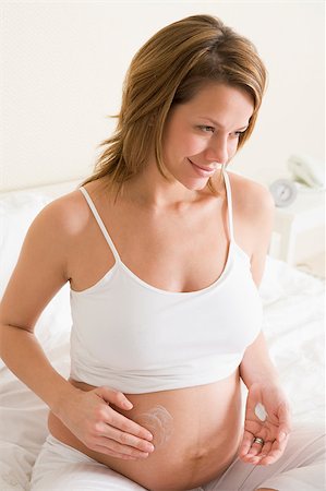 Pregnant woman in bedroom rubbing cream on belly smiling Stock Photo - Budget Royalty-Free & Subscription, Code: 400-04400456