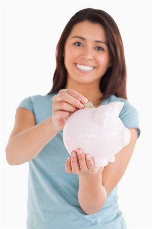 space money sign - Lovely woman inserting a coin in a piggy bank while standing against a white background Stock Photo - Budget Royalty-Free & Subscription, Code: 400-04416062