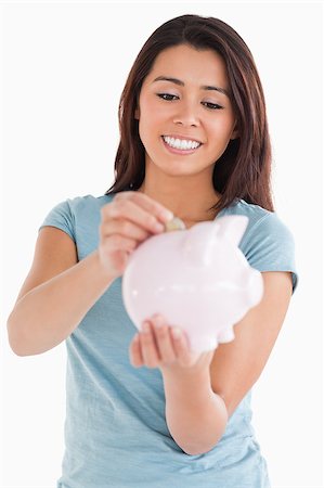 space money sign - Beautiful woman inserting a coin in a piggy bank while standing against a white background Stock Photo - Budget Royalty-Free & Subscription, Code: 400-04416063