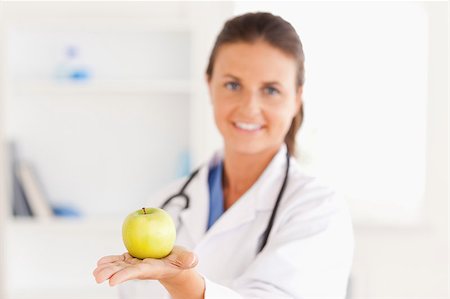 simsearch:400-05728493,k - Doctor with stethoscope holding an apple looking at the camera in the surgery Photographie de stock - Aubaine LD & Abonnement, Code: 400-04417388