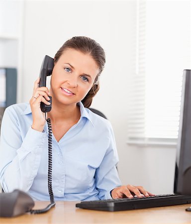 simsearch:400-04894274,k - A businesswoman is telephoning in an office while typing on a keyboard and looking into the camera Stock Photo - Budget Royalty-Free & Subscription, Code: 400-04417419