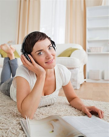 Portrait of a smiling woman with a magazine enjoying some music while lying on a carpet Stock Photo - Budget Royalty-Free & Subscription, Code: 400-04410787