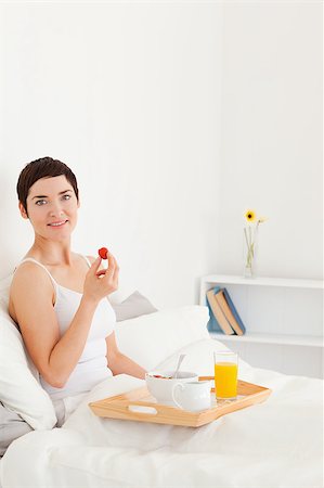 Portrait of a smiling brunette eating a strawberry in her bedroom Photographie de stock - Aubaine LD & Abonnement, Code: 400-04411052