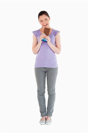 Lovely woman eating a chocolate block while standing against a white background Photographie de stock - Aubaine LD & Abonnement, Code: 400-04411207