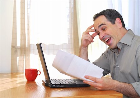 Man sitting at his desk with a laptop and papers looking happy Stock Photo - Budget Royalty-Free & Subscription, Code: 400-04437959