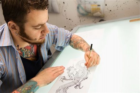 Caucasian male tattoo artist drawing tattoo on light table. Fotografie stock - Microstock e Abbonamento, Codice: 400-04445174