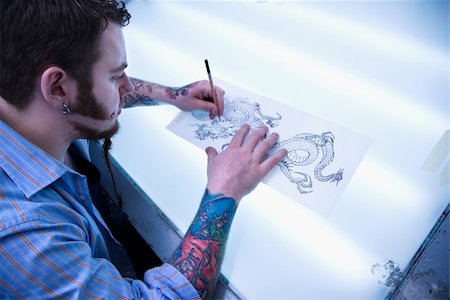 simsearch:400-03920996,k - Caucasian male tattoo artist drawing tattoo on light table. Photographie de stock - Aubaine LD & Abonnement, Code: 400-04445175