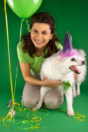simsearch:400-04446187,k - Caucasian prime adult female kneeling with fluffy white dog wearing party hat. Photographie de stock - Aubaine LD & Abonnement, Code: 400-04446196