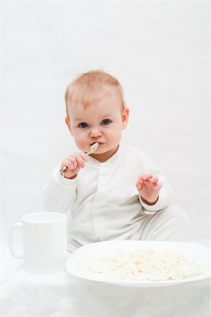 pictures of baby eating dinner with family - cute little girl sitting on white blanket with spoon in her hands. There are white plate with curd and white cup in front of her. Stock Photo - Budget Royalty-Free & Subscription, Code: 400-04440971