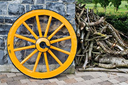 simsearch:400-05102252,k - An old antique yellow wooden wagon wheel leaning against a stone wall. There is a pile of tree branches laying next to it. Stock Photo - Budget Royalty-Free & Subscription, Code: 400-04455008