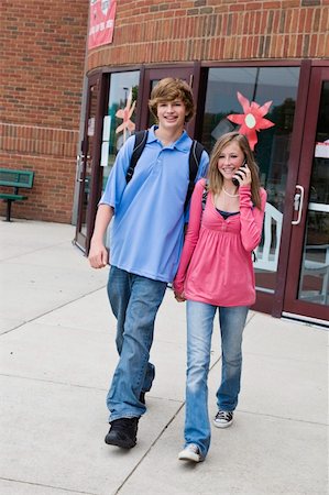 Young teenage boy and girl holding hands while walking and the girl is talking on cell phone outside of a school building Stock Photo - Budget Royalty-Free & Subscription, Code: 400-04456434