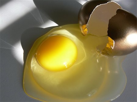 simsearch:400-04499320,k - Golden egg, broken open and leaking its contents across a white tabletop, with patterns of shadow and light across all. Taken with a Panasonic FZ30. Fotografie stock - Microstock e Abbonamento, Codice: 400-04457024