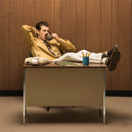 Caucasion mid-adult retro businessman sitting with feet propped on desk leaning back with hand behind head drinking coffee. Stock Photo - Budget Royalty-Free & Subscription, Code: 400-04450042