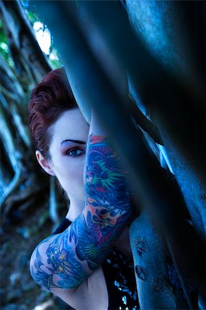 simsearch:400-04186416,k - Blue-toned portrait of tattooed Caucasian woman hiding behind Banyan tree in Maui, Hawaii, USA. Stockbilder - Microstock & Abonnement, Bildnummer: 400-04450864