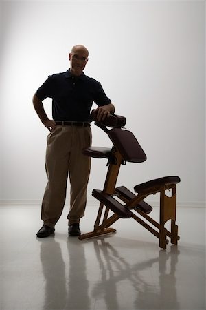 Silhouette of Caucasian middle-aged male massage therapist standing with elbow on massage chair. Stockbilder - Microstock & Abonnement, Bildnummer: 400-04451349