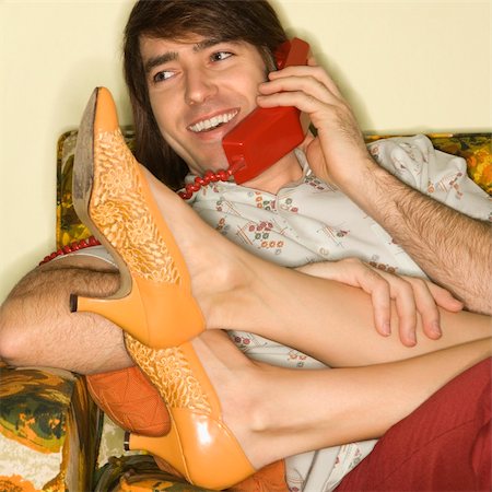 simsearch:400-04451365,k - Caucasian mid-adult man talking on telephone with Caucasion mid-adult woman's legs draped over lap. Foto de stock - Super Valor sin royalties y Suscripción, Código: 400-04451367