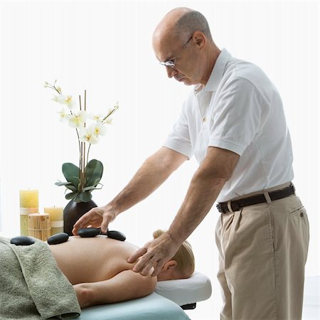 simsearch:400-04956215,k - Caucasian middle-aged male massage therapist placing hot stones on back of Caucasian middle-aged woman lying on massage table. Photographie de stock - Aubaine LD & Abonnement, Code: 400-04451360