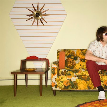 simsearch:400-04451365,k - Caucasian mid-adult man sitting on colorful retro sofa wearing sunglasses in room with vintage decor. Foto de stock - Super Valor sin royalties y Suscripción, Código: 400-04451363