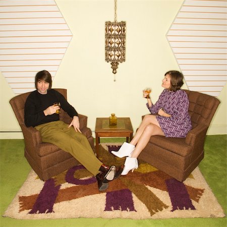 simsearch:400-04451365,k - Caucasian mid-adult man and woman wearing vintage clothing seated in brown retro chairs smiling and drinking. Foto de stock - Super Valor sin royalties y Suscripción, Código: 400-04451388