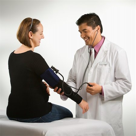 Asian American male doctor testing blood pressure of pregnant Caucasian woman. Stock Photo - Budget Royalty-Free & Subscription, Code: 400-04452038