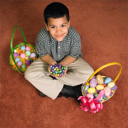simsearch:400-04452450,k - Hispanic boy sitting on floor with two Easter baskets holding chocolate candy eggs in his hands looking up at viewer smiling. Stock Photo - Budget Royalty-Free & Subscription, Code: 400-04452434