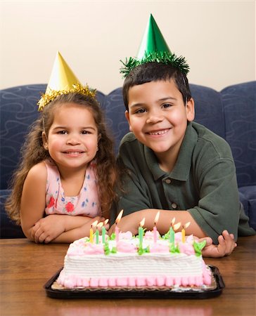 simsearch:400-04452450,k - Hispanic girl and boy wearing party hats sitting in front of birthday cake smiling and looking at viewer. Stock Photo - Budget Royalty-Free & Subscription, Code: 400-04452442
