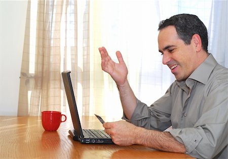 Man sitting at his desk with laptop holding a credit card looking happy Stock Photo - Budget Royalty-Free & Subscription, Code: 400-04452716