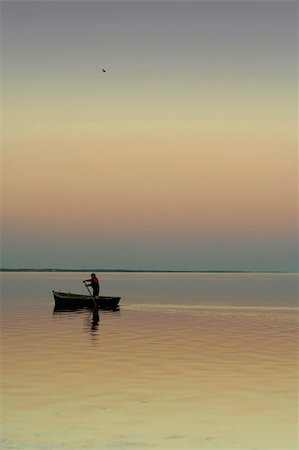 simsearch:400-04501989,k - Lonely boat on silent water. Sunset. Beautiful reflection in water. One the man in a boat and one bird in the sky. The excellent quiet photo. Stockbilder - Microstock & Abonnement, Bildnummer: 400-04474134